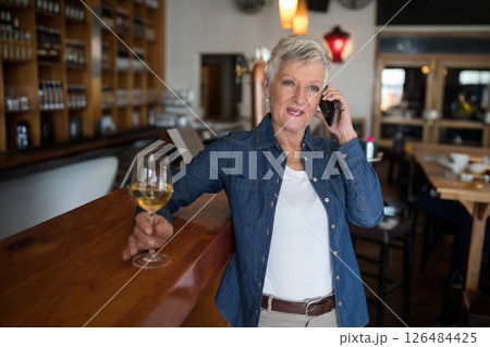 Mature woman enjoying wine while talking on smartphone at cozy bar, copy space 126484425