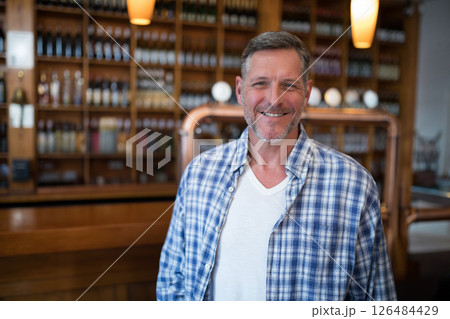 Smiling man in plaid shirt standing at bar with wine bottles in background, copy space Smiling man in plaid shirt standing at bar with wine bottles in background, copy space 126484429