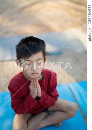 Young boy meditating on yoga mat outdoors, practicing mindfulness and relaxation, copy space 126484435