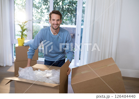 Smiling man packing boxes at home, preparing for move with bubble wrap, copy space 126484440