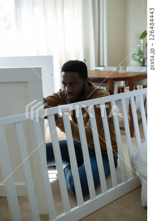 Man assembling baby crib in bedroom, concentrating on task with determination, copy space 126484443