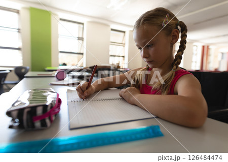 In school, young girl with braids writing in notebook at classroom desk, copy space In school, young girl with braids writing in notebook at classroom desk, copy space 126484474