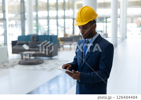 Engineer in suit using tablet in modern office building, focused on work, copy space Engineer in suit using tablet in modern office building, focused on work, copy space 126484484