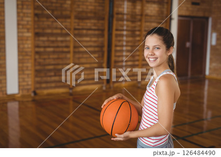 Smiling girl holding basketball in school gym, ready for practice, copy space 126484490