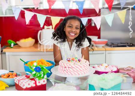 Smiling girl celebrating birthday at home with cake and colorful decorations Smiling girl celebrating birthday at home with cake and colorful decorations 126484492