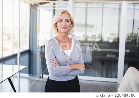Confident businesswoman standing in modern office, arms crossed, looking determined 126484500