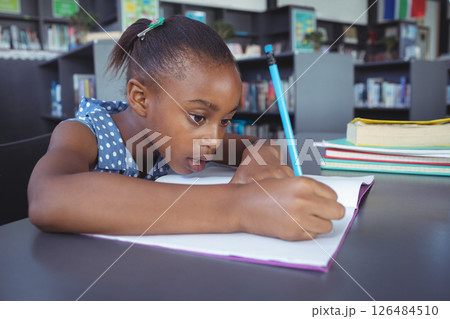 In school, focused girl writing in notebook at library table, concentrating hard 126484510