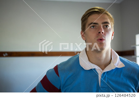 Young man in blue rugby jersey looking focused and determined indoors, copy space 126484520