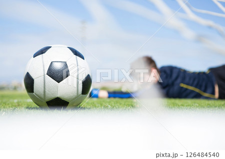 Soccer ball on field with player in background reaching for goal, copy space 126484540