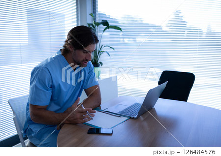 Healthcare professional in scrubs using laptop and smartphone in modern office, copy space 126484576
