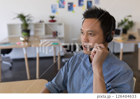 Asian man using headset working in modern office, engaging in conversation, copy space 126484633