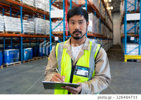 Warehouse worker in safety vest checking inventory on clipboard, ensuring accuracy 126484733