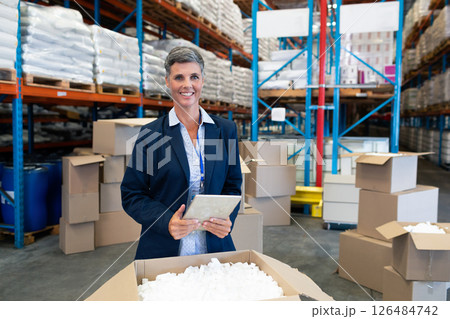 Smiling businesswoman using tablet in warehouse surrounded by boxes and shelves, copy space Smiling businesswoman using tablet in warehouse surrounded by boxes and shelves, copy space 126484742