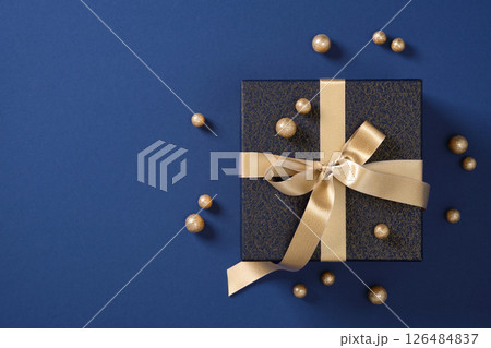 Dark blue gift box with gold ribbon and decorations on a blue background. Space for your text. Dark blue gift box with gold ribbon and decorations on a blue background. Space for your text. 126484837
