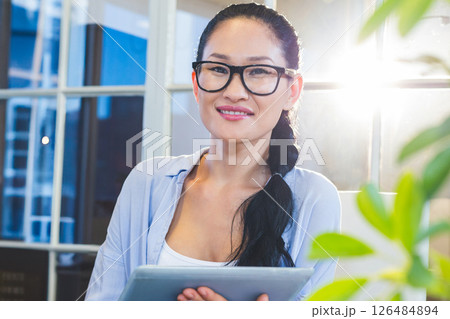Confident businesswoman holding tablet in bright modern office, smiling warmly 126484894