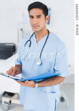 In hospital, medical professional in scrubs reviewing patient chart with stethoscope 126484895