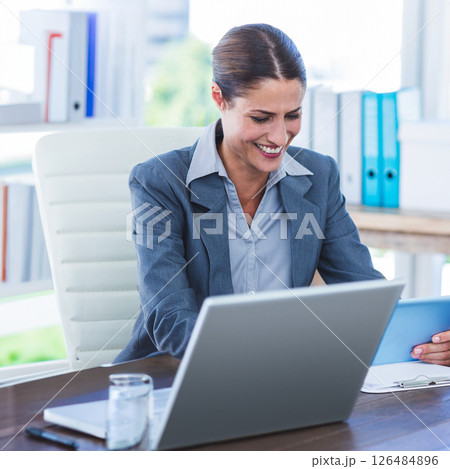 Businesswoman smiling while using laptop and tablet in modern office Businesswoman smiling while using laptop and tablet in modern office 126484896