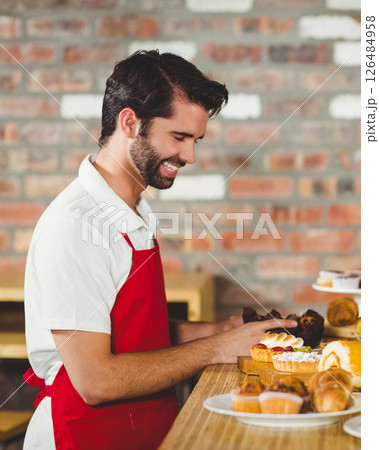 Barista in red apron arranging pastries with smile at cozy café counter 126484958