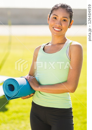 Smiling woman holding yoga mat outdoors, ready for morning exercise routine Smiling woman holding yoga mat outdoors, ready for morning exercise routine 126484959