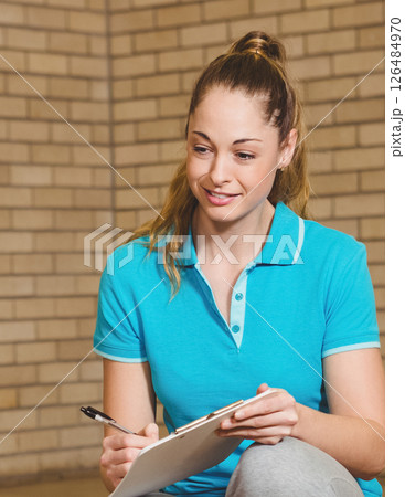 Smiling teacher taking notes on clipboard in school gym, wearing blue polo 126484970