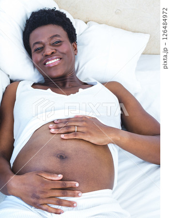 Pregnant woman relaxing on bed, smiling and embracing her belly with joy 126484972