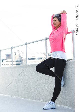 Woman stretching on rooftop, wearing pink sweatshirt, enjoying urban fitness routine, copy space 126484979