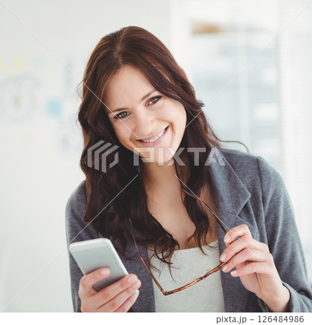 Smiling woman holding smartphone and glasses, enjoying work at office 126484986