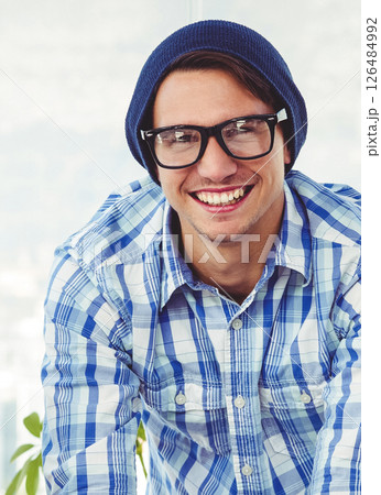 Smiling hipster man wearing glasses and beanie in casual office setting Smiling hipster man wearing glasses and beanie in casual office setting 126484992