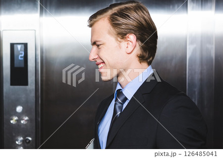Businessman smiling confidently in elevator, holding clipboard, wearing formal suit 126485041