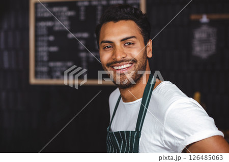 Smiling barista in apron welcoming customers at cozy coffee shop counter 126485063