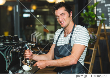 Barista making coffee, smiling while preparing espresso in cozy coffee shop Barista making coffee, smiling while preparing espresso in cozy coffee shop 126485068