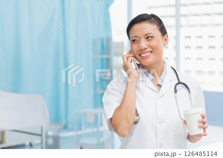 Asian female doctor smiling while talking on phone, holding coffee in hospital, copy space 126485114