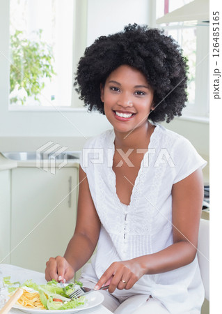 Smiling woman enjoying healthy salad in bright kitchen at home Smiling woman enjoying healthy salad in bright kitchen at home 126485165