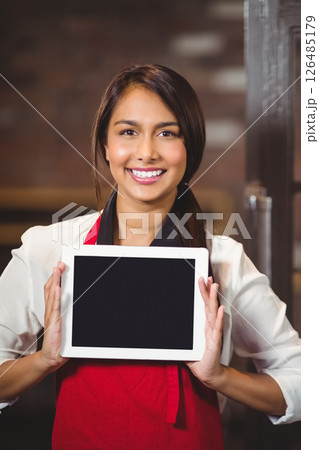 Smiling woman in red apron holding tablet in cozy café environment, copy space Smiling woman in red apron holding tablet in cozy café environment, copy space 126485179