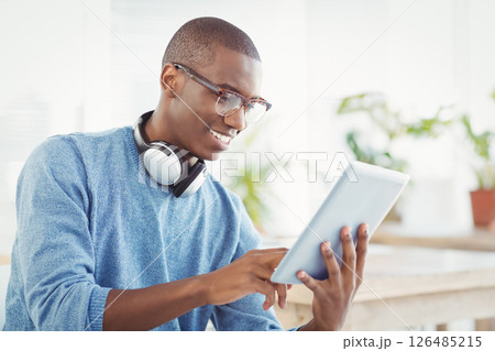 African American man using tablet with headphones, smiling and working at office African American man using tablet with headphones, smiling and working at office 126485215