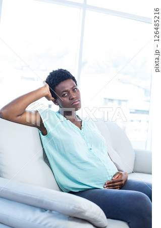 Pregnant woman relaxing on sofa at home, hand resting on belly 126485216