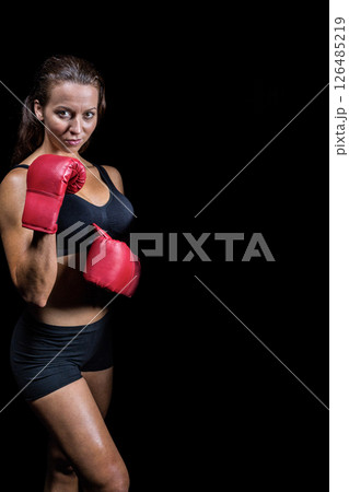 Confident woman in red boxing gloves posing against black background, copy space 126485219
