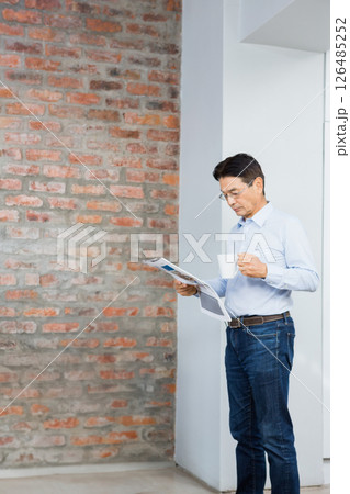 Asian man reading newspaper and drinking coffee at home, enjoying morning routine, copy space Asian man reading newspaper and drinking coffee at home, enjoying morning routine, copy space 126485252