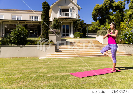 Woman practicing yoga on pink mat in front of beautiful house, enjoying tranquility, copy space 126485273