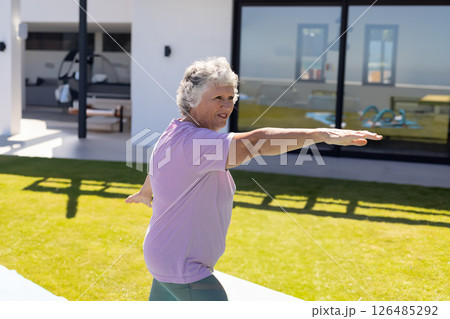 Senior woman practicing yoga outdoors on sunny day, stretching arms on mat, copy space 126485292