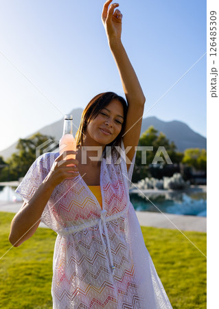 Smiling woman enjoying refreshing drink by pool, raising arm in relaxation, copy space Smiling woman enjoying refreshing drink by pool, raising arm in relaxation, copy space 126485309
