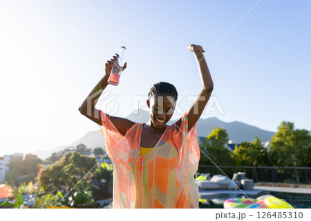 Joyful woman dancing by pool, holding drink, enjoying sunny day outdoors, copy space Joyful woman dancing by pool, holding drink, enjoying sunny day outdoors, copy space 126485310