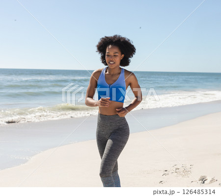 African American woman jogging on beach, enjoying sunny day and ocean breeze, copy space 126485314