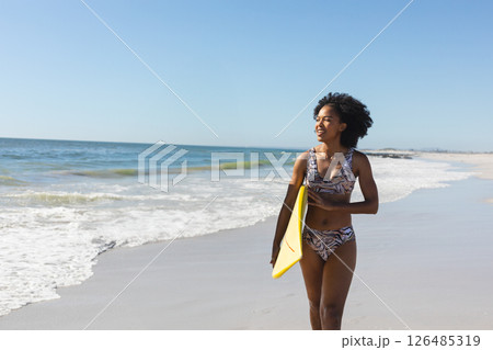 Woman in swimsuit holding surfboard walking along beach, enjoying sunny day, copy space Woman in swimsuit holding surfboard walking along beach, enjoying sunny day, copy space 126485319
