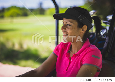 Smiling woman in pink polo shirt enjoying golf cart ride on sunny day, copy space 126485329