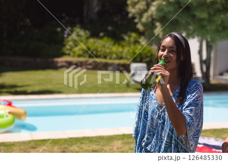 Young woman enjoying cold drink by pool, smiling and relaxing at outdoor party, copy space Young woman enjoying cold drink by pool, smiling and relaxing at outdoor party, copy space 126485330