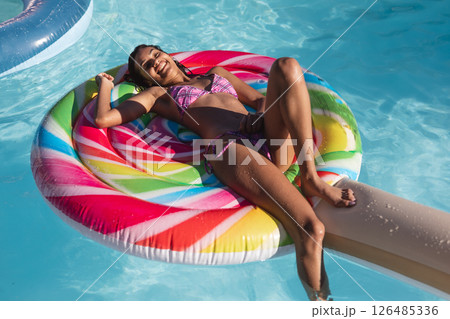 Smiling woman relaxing on colorful pool float, enjoying sunny day at pool party, copy space 126485336