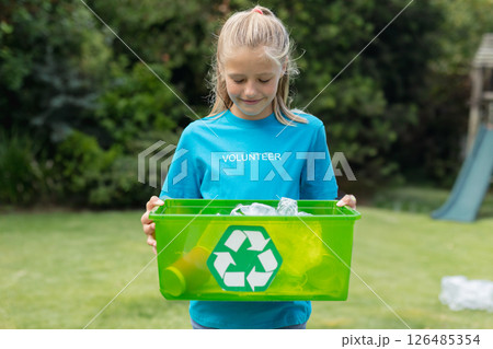 Young girl volunteering, holding green recycling bin outdoors, smiling at task, copy space Young girl volunteering, holding green recycling bin outdoors, smiling at task, copy space 126485354