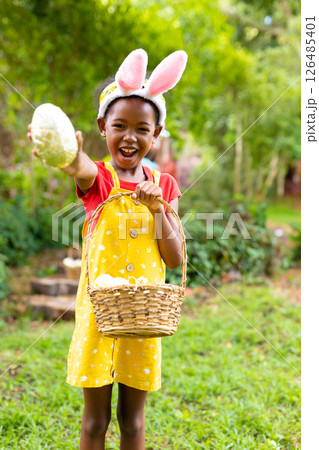 Child in garden wearing bunny ears holding egg and basket, celebrating Easter Child in garden wearing bunny ears holding egg and basket, celebrating Easter 126485401