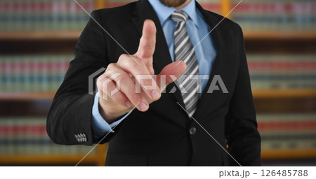 Businessman in suit pointing at camera in office with bookshelves behind 126485788